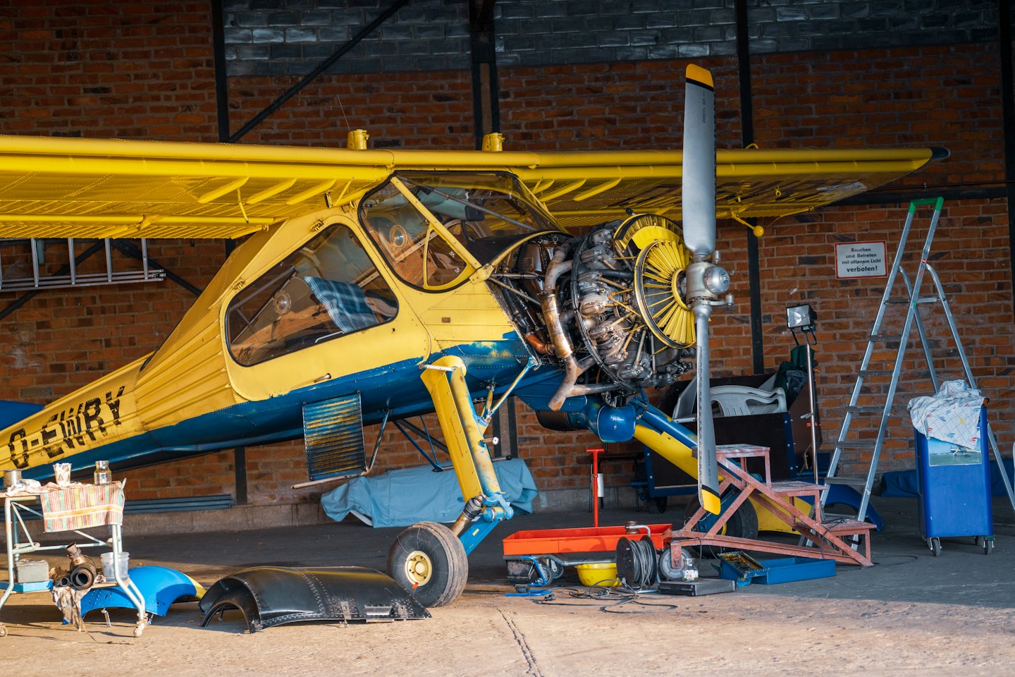 Mechanik serwisuje żółto-niebieski samolot w hangarze.